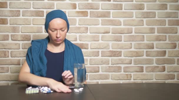En kvinna i en huvudduk, en cancerpatient, berör piller, sitter vid ett bord mot en tegelvägg. Kopiera utrymme — Stockvideo