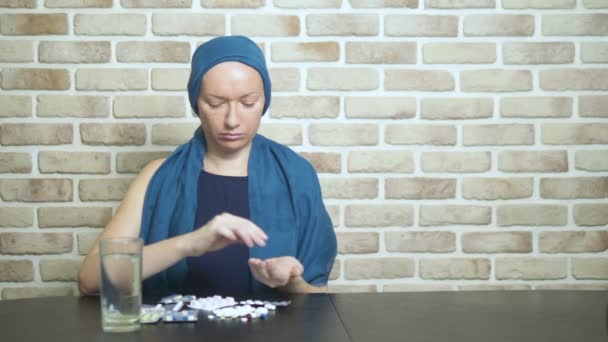 Uma mulher em um lenço de cabeça, um paciente com câncer, toca pílulas, sentado em uma mesa contra uma parede de tijolo. espaço de cópia — Vídeo de Stock