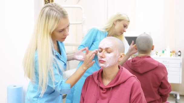 Стильная лысая женщина на приеме у косметолога. нанесение обезболивающего крема на лицо — стоковое видео