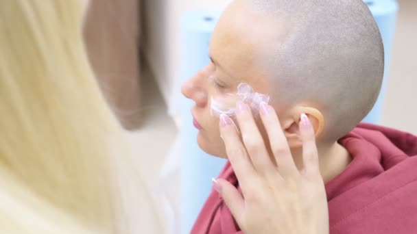 Stílusos kopasz nő egy kozmetikus kinevezését. érzéstelenítő krém alkalmazása az arcra — Stock videók