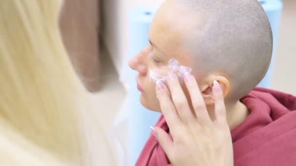 Mulher careca elegante em uma nomeação esteticista. aplicação de creme anestésico no rosto — Vídeo de Stock