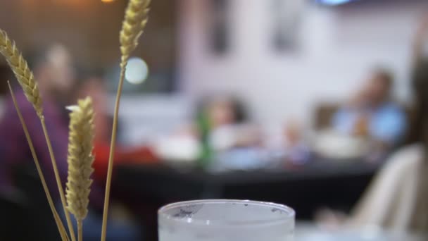 Close-up. oren van tarwe en bierglas op een onscherpe achtergrond mensen aan tafel — Stockvideo