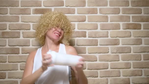 Menina alegre feliz com cabelo encaracolado branco curto treme sua coqueteleira em um fundo de parede de tijolo. espaço de cópia — Vídeo de Stock