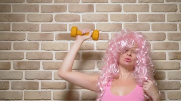 Chica loca con el pelo rizado rosa demuestra sus bíceps contra una pared de ladrillo. espacio de copia. concepto de humor, aventuras de gente extraña . — Vídeos de Stock