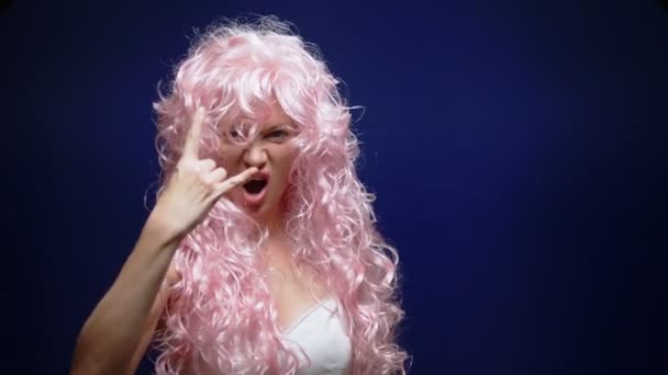 Mooi gek meisje met lange roze krullend haar toont Rock teken met haar hand op een donkere achtergrond — Stockvideo