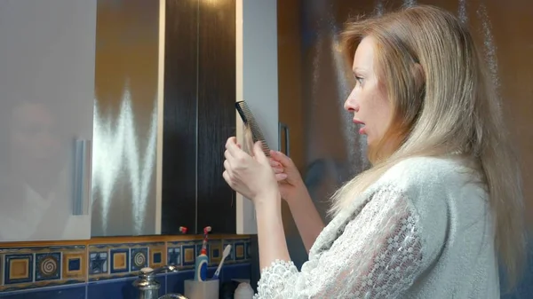 Alopecia, calvicie. la rubia se peina el pelo en el baño y un mechón de pelo permanece en el lavabo. espacio de copia — Foto de Stock