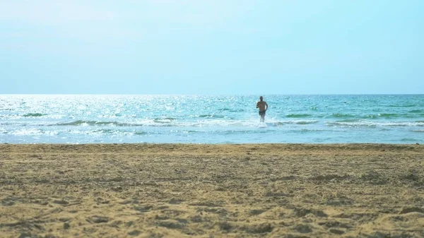 Junger Mann läuft an einem Sandstrand auf See — Stockfoto