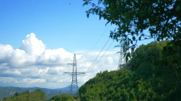 Kraftledningar bland berg och träd mot himlen. Kopiera utrymme — Stockfoto