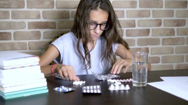 sağlık kavramı, eğitim yükleri sırasında avitominoz. genç kız ders kitapları ve notlar ile bir masada oturan hapları sıralama