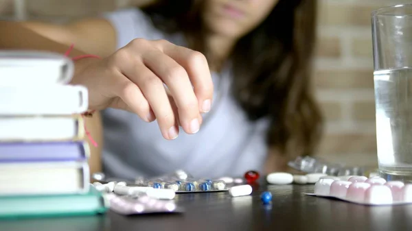 Nahaufnahme von Händen, die Tabletten berühren. Gesundheitskonzept, beriberi während der Trainingsbelastung. Teenager-Mädchen sortiert Pillen am Tisch mit Schulbüchern und Notizen — Stockfoto