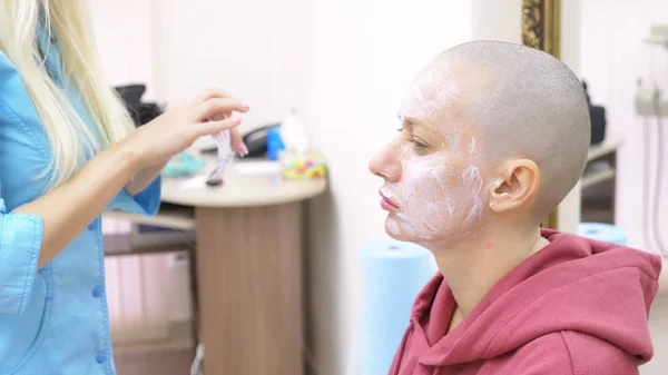 Stylish bald woman at a beautician appointment. applying anesthetic cream to the face — Stock Photo, Image