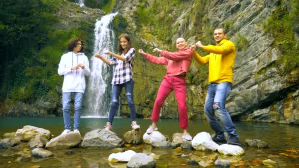Skallig kvinna hennes barn och make dansar mot bakgrund av ett vattenfall, tittar på kameran. — Stockvideo
