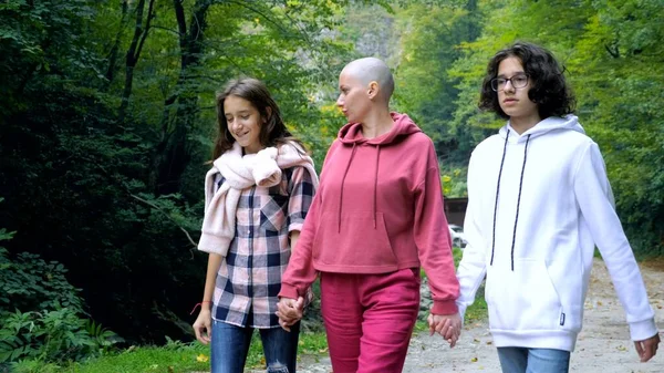 Skallig kvinna, mor och hennes tonåriga barn går tillsammans i en park eller skog — Stockfoto