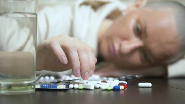 Közelkép. Egy fiatal kopasz nő szomorúan nézi a tablettákat, miközben egy asztalnál ül egy téglafalnak támasztva. másolás helye — Stock Fotó
