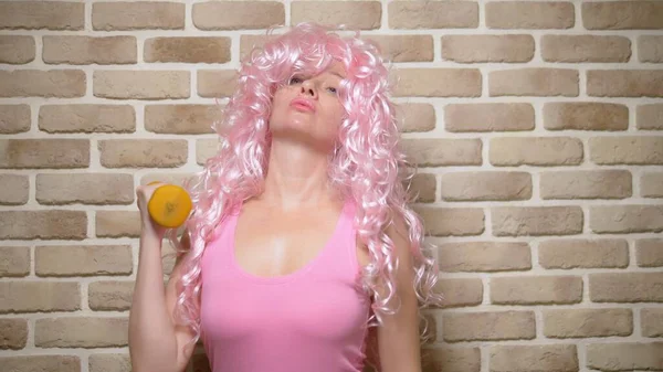 Menina louca com cabelo encaracolado rosa demonstra seu bíceps contra uma parede de tijolo. espaço de cópia. conceito de humor, aventuras de pessoas estranhas . — Fotografia de Stock
