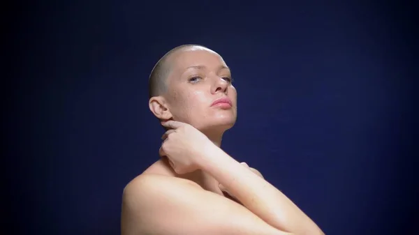 Emotional portrait of a beautiful bald woman with bare shoulders against a dark background. she is touching her head and neck with her hands. — Stock Photo, Image