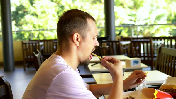 Πεινασμένος άνθρωπος τρώει τηγανιτές πατάτες σε ένα εστιατόριο fast food. κοντινό πλάνο. — Φωτογραφία Αρχείου