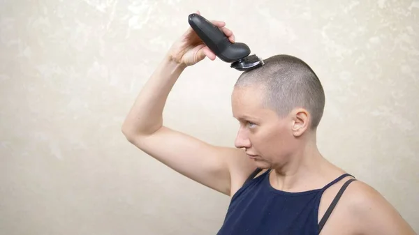 En skallig kvinna rakar huvudet med en elektrisk rakkniv. närbild, kopiera utrymme — Stockfoto