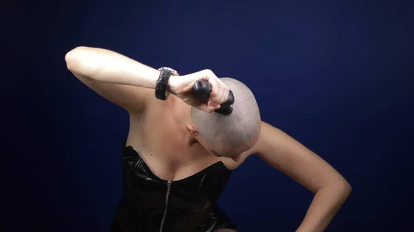 Une femme chauve sexy cool dans un corset en cuir se rase la tête avec un rasoir électrique sur un fond sombre. espace de copie. aventures de gens étranges . — Photo