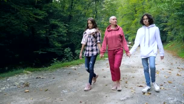Bald woman, mother and her teenage children walk together in a park or forest — Stock Video