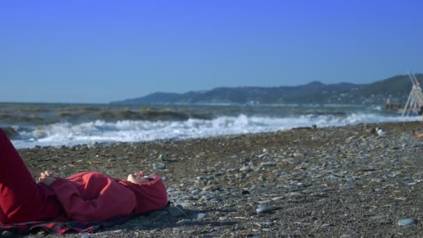 Flicka i en tröja och solglasögon ligger på stranden under en storm. — Stockvideo
