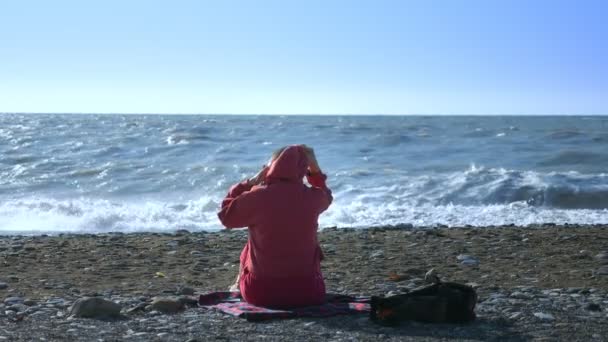 Φαλακρή γυναίκα με μπλούζα κάθεται στην παραλία κατά τη διάρκεια μιας καταιγίδας.. — Αρχείο Βίντεο