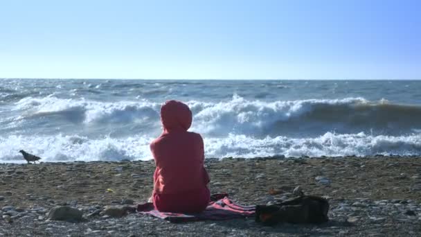 Tişörtlü kel bir kadın fırtına sırasında deniz kıyısında oturur.. — Stok video