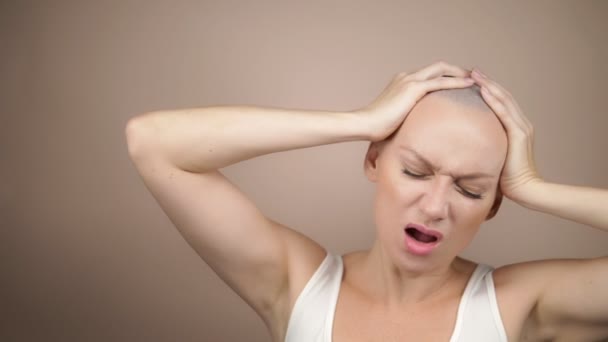 Bald woman holds her hands behind her head and screams. beige background, copy space — Stock Video