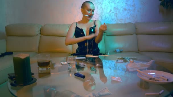 Роскошная лысая женщина в черном кожаном корсете вводит наркотики, сидя на диване в гостиной — стоковое видео