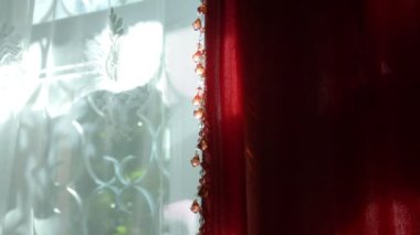 Güneşli bir günde penceredeki güzel kırmızı ve beyaz perdeler. Dekorun boncuklarında güneşli bir parıltı.