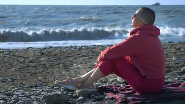 Skallig kvinna i tröja sitter på stranden under en storm. — Stockvideo