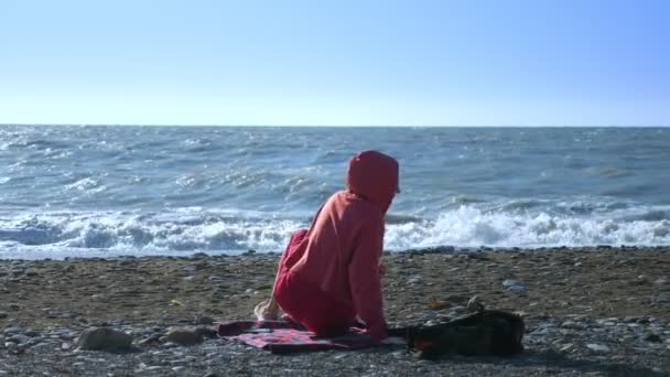 Flicka i en tröja och solglasögon ligger på stranden under en storm. — Stockvideo