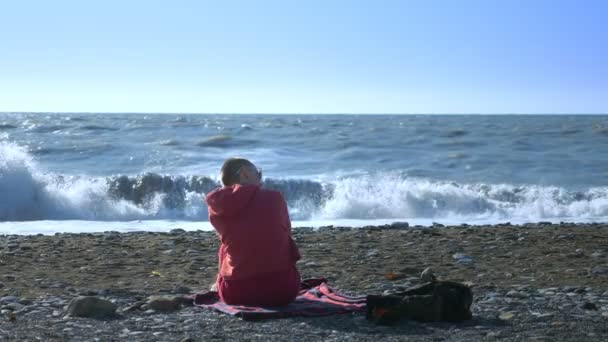 Skallig kvinna i tröja sitter på stranden under en storm. — Stockvideo