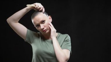 Tişörtlü bir asker kız siyah arka planda tehlikeli bir jiletle kafasını tıraş ediyor.