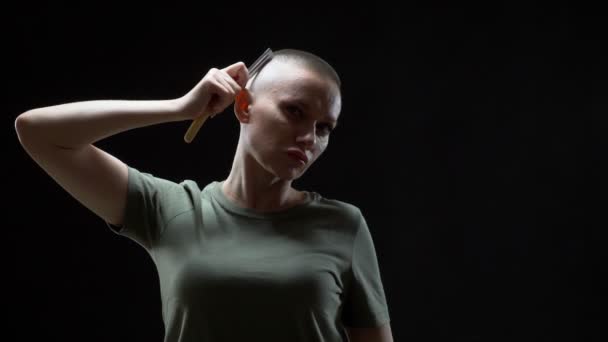 Militar chica en una camiseta se afeita la cabeza con una navaja peligrosa sobre un fondo negro — Vídeos de Stock