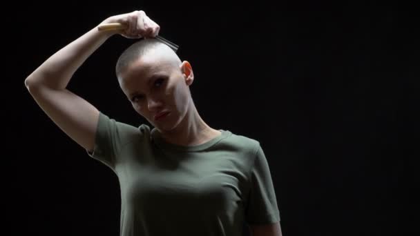 Ragazza militare in una t-shirt si rasa la testa con un rasoio pericoloso su uno sfondo nero — Video Stock