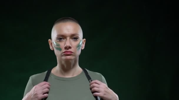 Portrét holohlavé ženy ve vojenském maskovacím make-upu a postroji, jak se dívá do kamery a pózuje. kopírovat prostor — Stock video