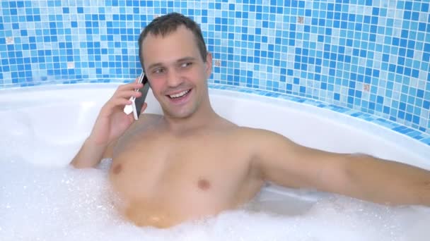 Молодой человек бросает сотовый телефон в воду, принимая ванну — стоковое видео