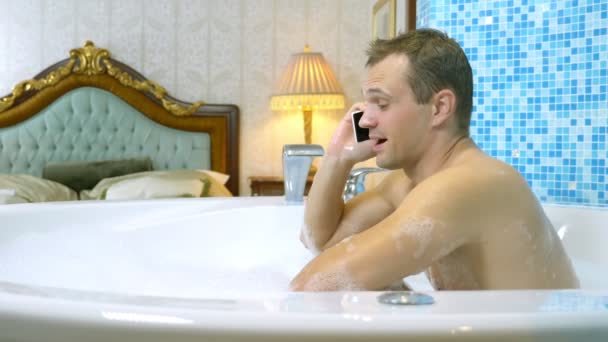 Een jongeman gooit een mobieltje in het water terwijl hij een bad neemt — Stockvideo