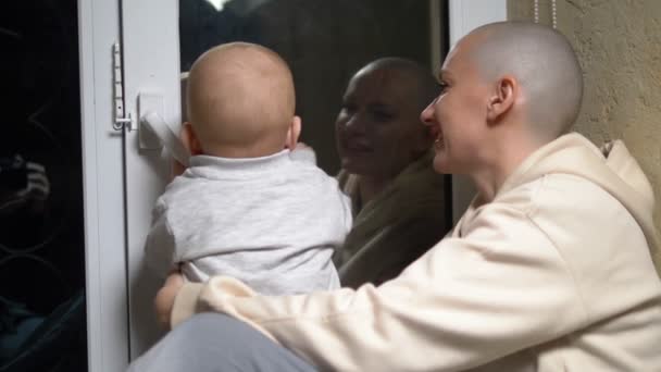 Careca mulher e bebê sentar juntos na janela à noite.close-up — Vídeo de Stock