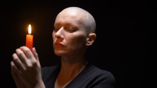 Portrait of a bald woman with a candle on a black background. copy space — Stock Video