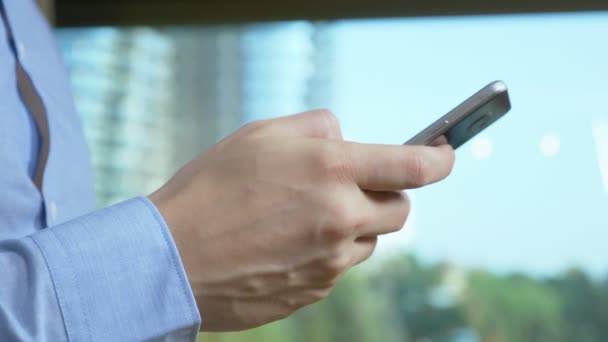 Nahaufnahme. Männliche Hände benutzen das Telefon vor dem Hintergrund eines Fensters, aus dem Wolkenkratzer zu sehen sind — Stockvideo