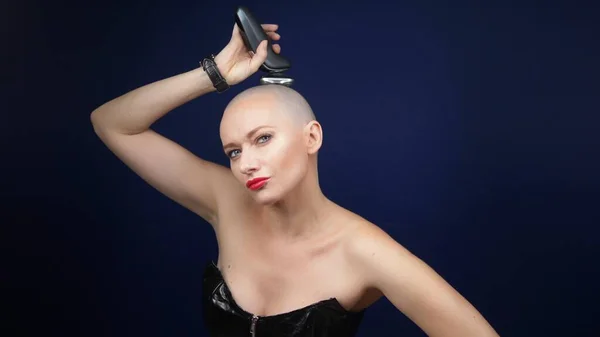 A cool sexy bald woman in a leather corset shaves her head with an electric razor against a dark background. copy space. adventures of strange people. — Stock Photo, Image