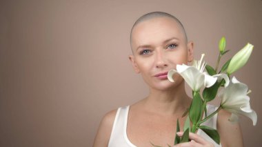 Güzel, gülümseyen kel kız beyaz bir zambak kokluyor. bej arkaplan, kopyalama alanı