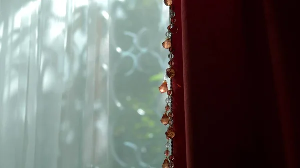 Beaux rideaux rouges et blancs sur la fenêtre par une journée ensoleillée claire. éblouissement ensoleillé sur les perles du décor . — Photo