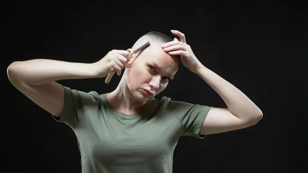 Στρατιωτική κοπέλα με μπλουζάκι ξυρίζει το κεφάλι της με ένα επικίνδυνο ξυράφι σε μαύρο φόντο. — Φωτογραφία Αρχείου