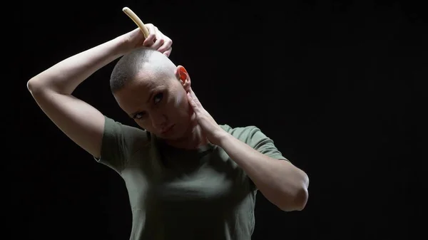 Military girl in a T-shirt shaves her head with a dangerous razor on a black background — Stock Photo, Image