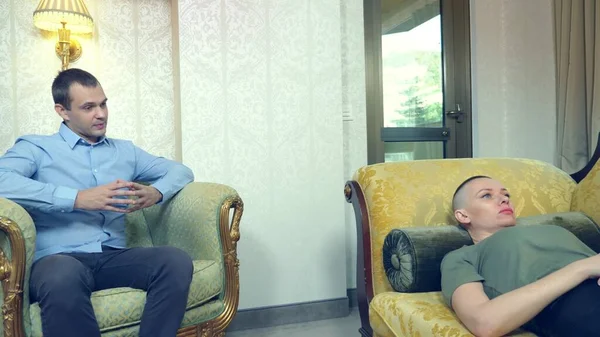 Психолог працює з молодою лисою жінкою, що лежить на дивані в стильному офісі — стокове фото