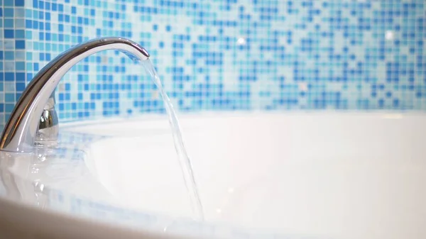 Primo piano. l'acqua scorre da un lussuoso rubinetto d'acqua in una grande vasca da bagno moderna contro una parete a mosaico blu — Foto Stock