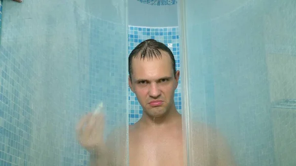 Ein Mann schaut in die Kamera, während er sich die Haare mit Shampoo wäscht und duscht — Stockfoto
